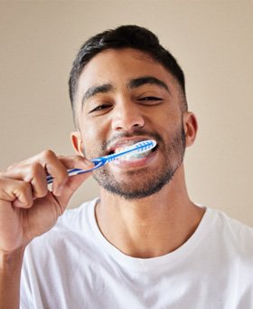 Man smiling while brushing his teeth